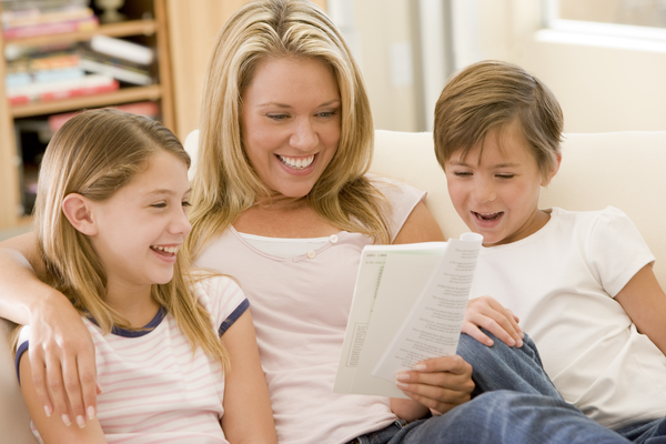Woman And Two Young Children In Living Room Reading Book And Smiling Sbi 301053903 (1)